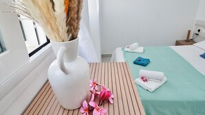 Une chambre d’hôtel avec un lit, une table de chevet, un vase contenant des plantes séchées et une fenêtre avec des stores.