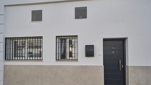 Un bâtiment doté de deux fenêtres avec des barreaux en métal, d’une porte noire avec une plaque nominative et de deux petites ouvertures dans le mur.