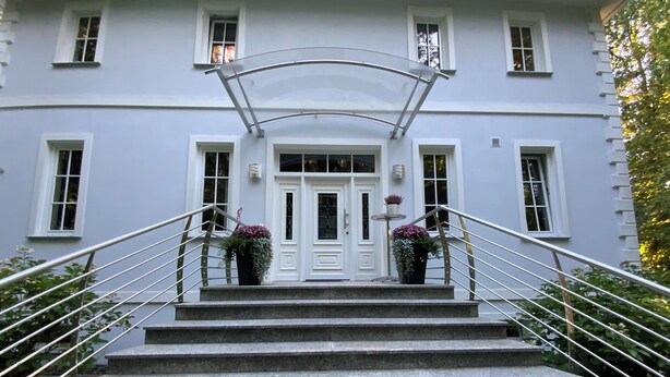 A building with a white facade, a central entrance with a double door, and a staircase with metal railings leading up to the entrance. - Cozy, quiet guest room with bathroom in a dream villa on the edge of the forest (Michendorf)