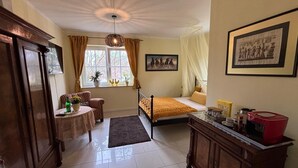 A room with a bed, a table with chairs, a window with curtains, a painting on the wall, and a cabinet. - Cozy, quiet guest room with bathroom in a dream villa on the edge of the forest (Michendorf)