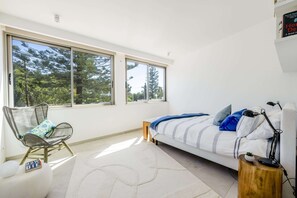 A bedroom with a bed, a chair, a small table, and large windows. - Luxury villa just steps from the beach | Heated pool, ocean views, and rooftop lounge   (Luz)