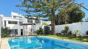 Une maison moderne avec une piscine, un grand arbre et une clôture blanche.