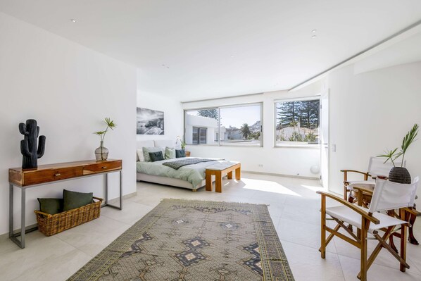 A modern living room with a large bed, a dining area, and a view of the outdoors. - Luxury Villa Steps from the Beach | Heated Pool, Ocean Views & Rooftop Lounge (Luz)