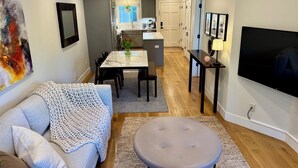 Een moderne woonkamer met een bank, een poef en een eethoek met een tafel en stoelen.