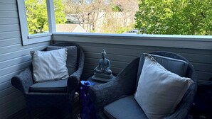 Een veranda met twee rieten stoelen, een bijzettafeltje en een Boeddhabeeld.