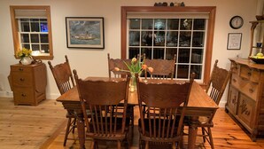 Comedor con una mesa y sillas de madera, un jarrón con flores y una ventana con vista a un barco.