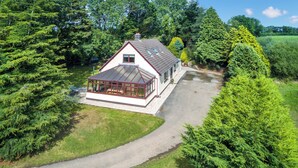 A house with a glass conservatory, surrounded by lush greenery and a paved driveway. - Dyffryn Conin is more than just a place to stay. (Clynderwen)