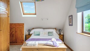 A bedroom with a wooden bed, a nightstand, a wardrobe, a skylight, and a window. - Dyffryn Conin is more than just a place to stay. (Clynderwen)
