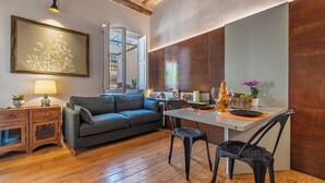 A modern living room with a grey sofa, wooden floor, a dining table with chairs, a lamp, and a large framed artwork. - Delightful Penthouse in the heart of Monti within walking distance metro Cavour and Colosseum. (Roma)