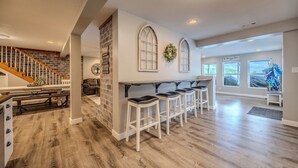 Una cocina amplia con escalera de madera, una barra con taburetes y vista al salón.