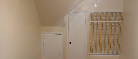Un espacio habitable compacto con sofá, una mesita, ventilador de techo, una puerta y una ventana con persianas.