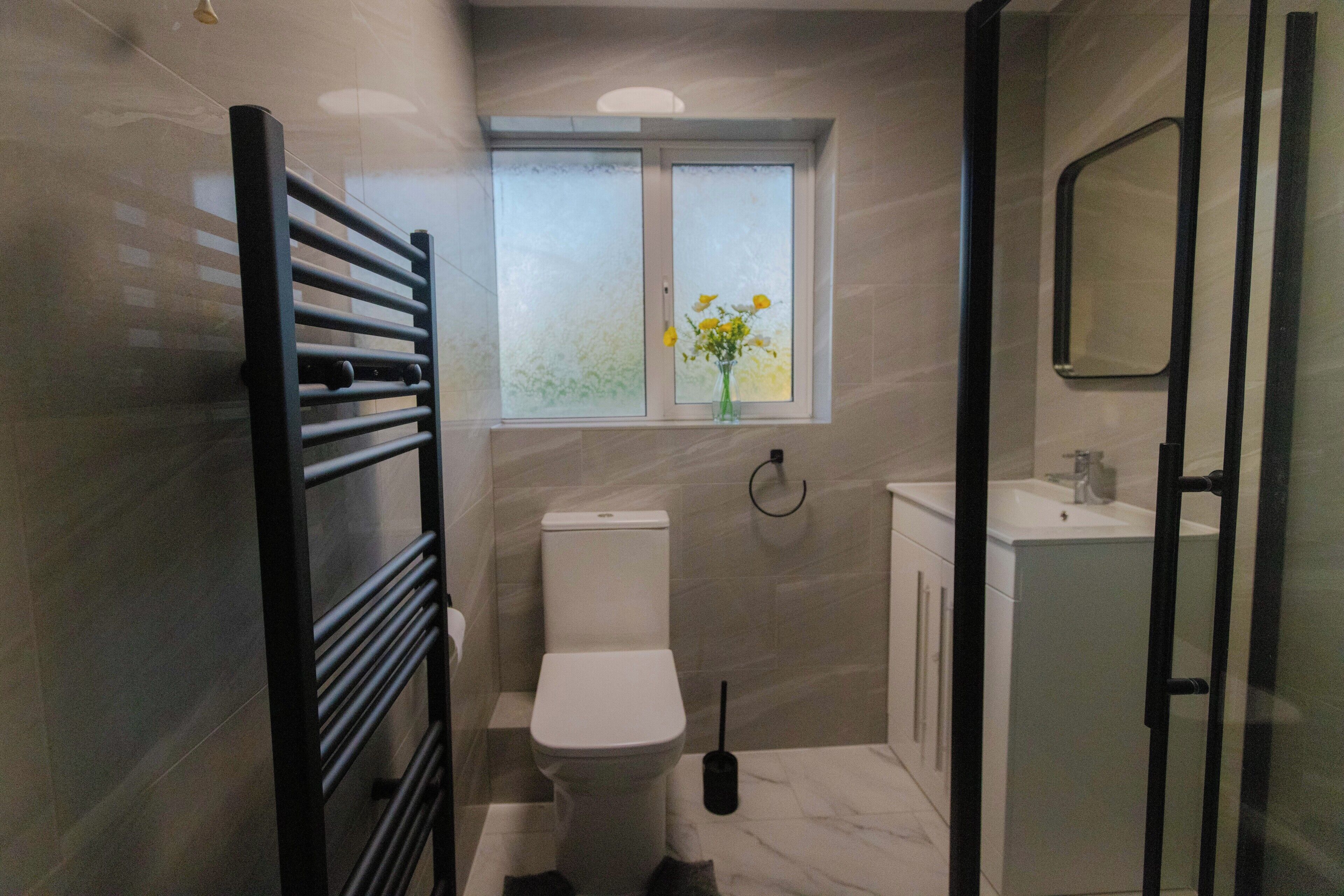 Ein modernes Badezimmer mit Toilette, einem Fenster mit Blumen in einer Vase, einem Handtuchhalter und einem Waschbecken.