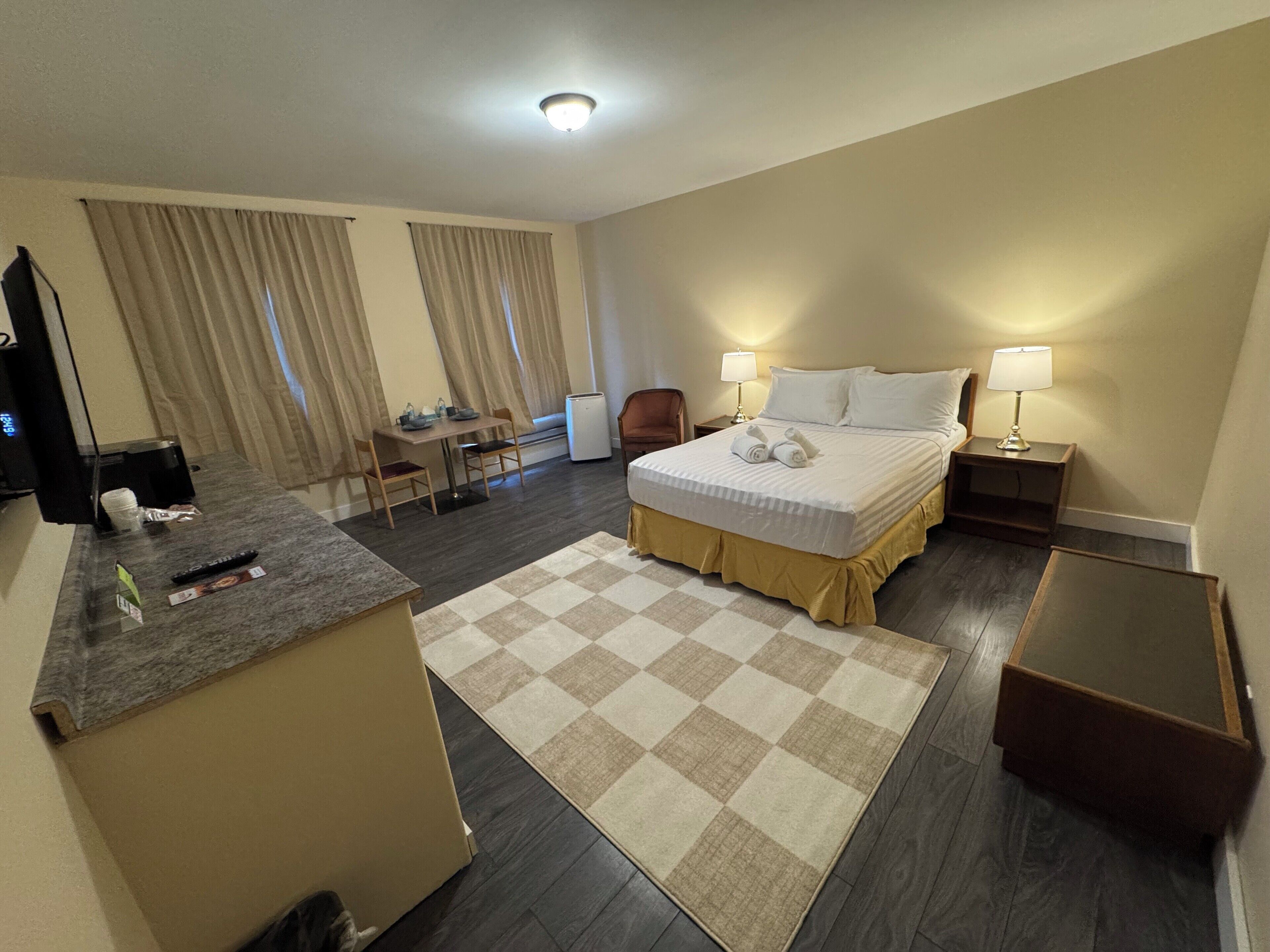 Une chambre d’hôtel comprenant un lit, des tables de chevet, un bureau avec une chaise, une télévision et un tapis à carreaux.