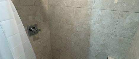A shower with a square showerhead, a tiled wall, and a white shower curtain.