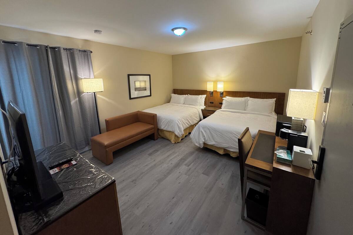 A hotel room with two beds, a desk, a TV, and a couch.