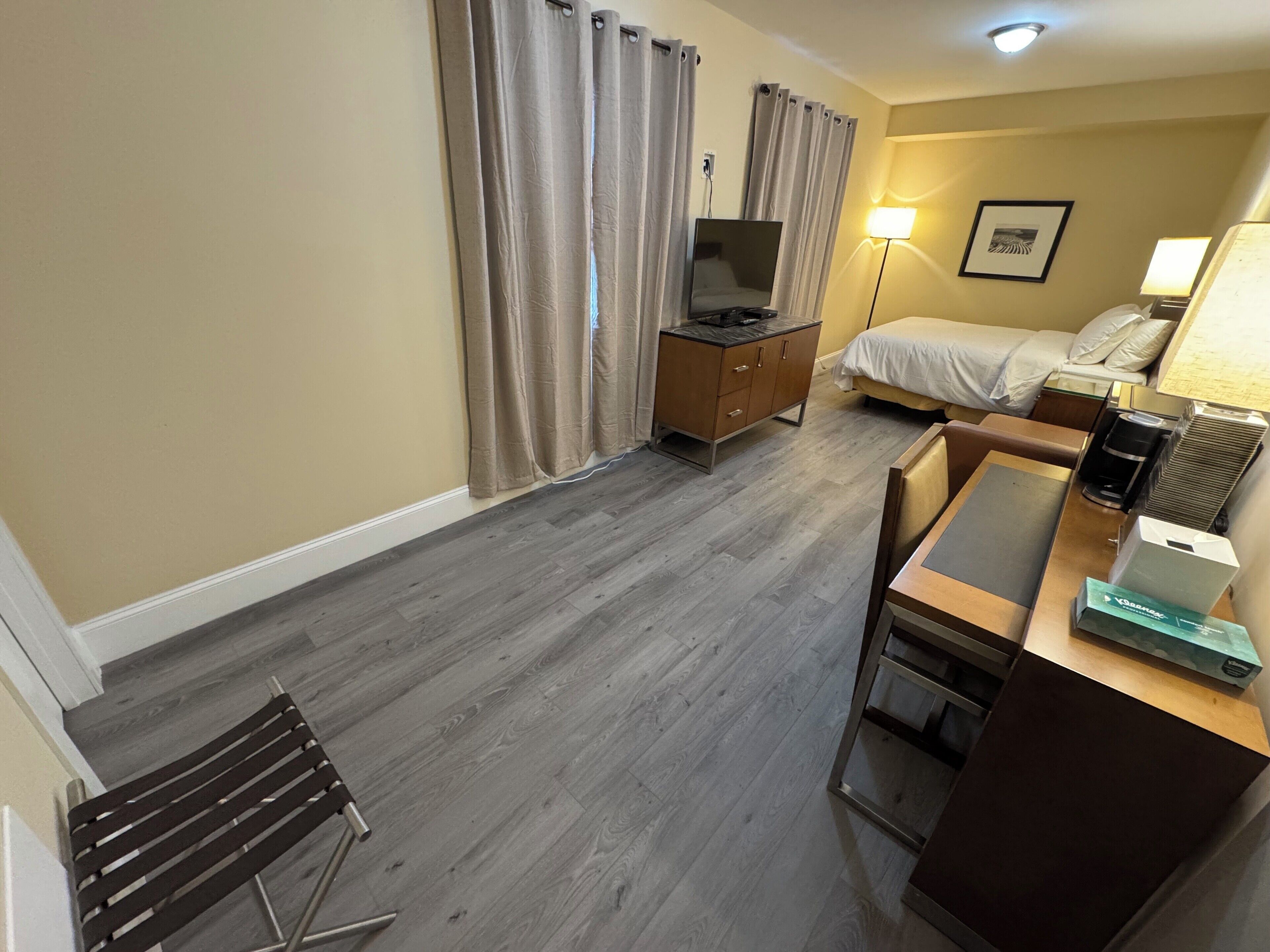 A hotel room with a bed, a desk with a computer, a TV, a dresser, and a lamp.