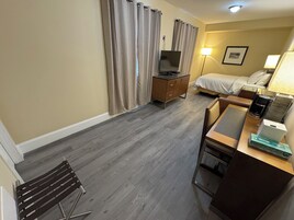 A hotel room with a bed, a desk with a computer, a TV, a dresser, and a lamp.