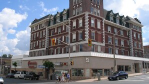 A multi-story hotel with a prominent corner location, featuring a mix of brick and stone facades, large windows, and a flat roof. - Kenricia Hotel (Kenora)