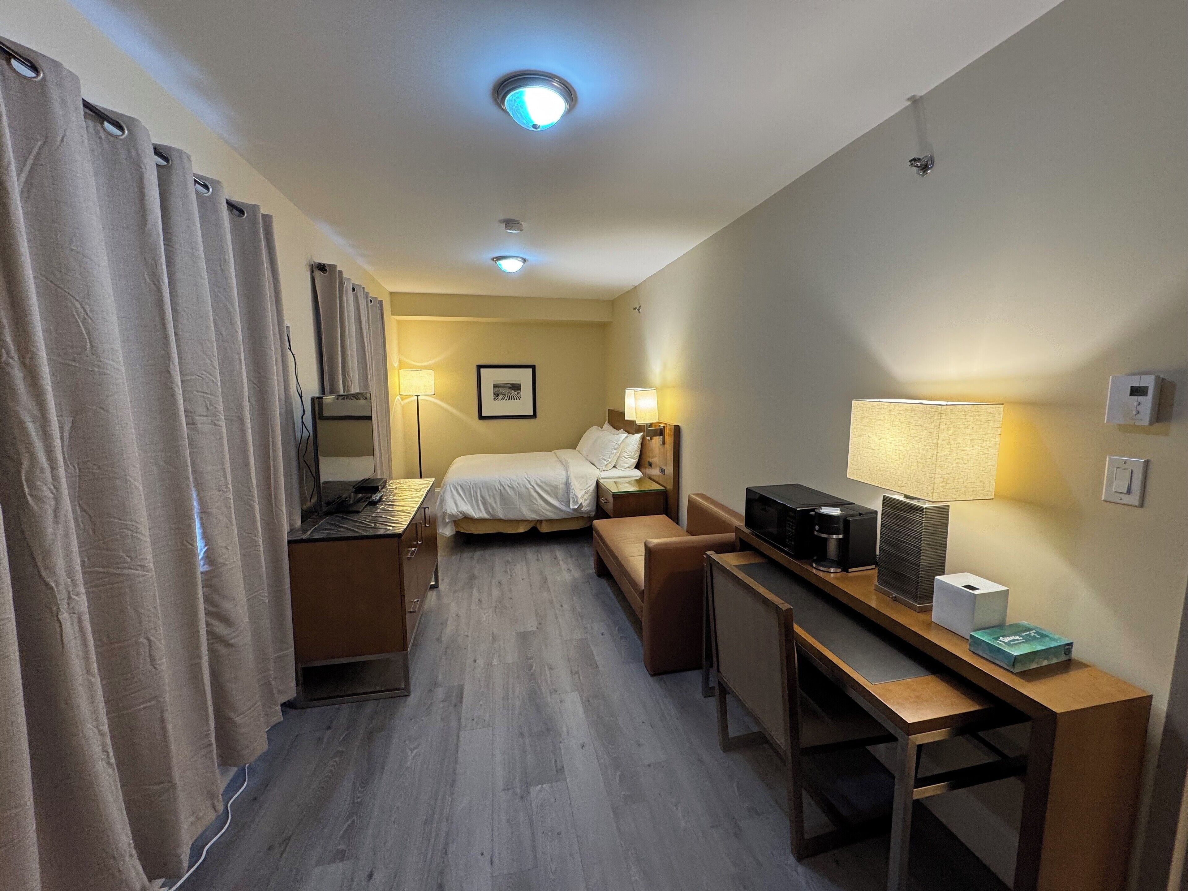 A hotel room with a bed, desk, chair, and a TV.