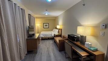 A hotel room with a bed, desk, chair, and a TV.