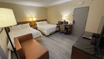 A hotel room with two beds, a desk with a computer, a chair, a TV, and a lamp.