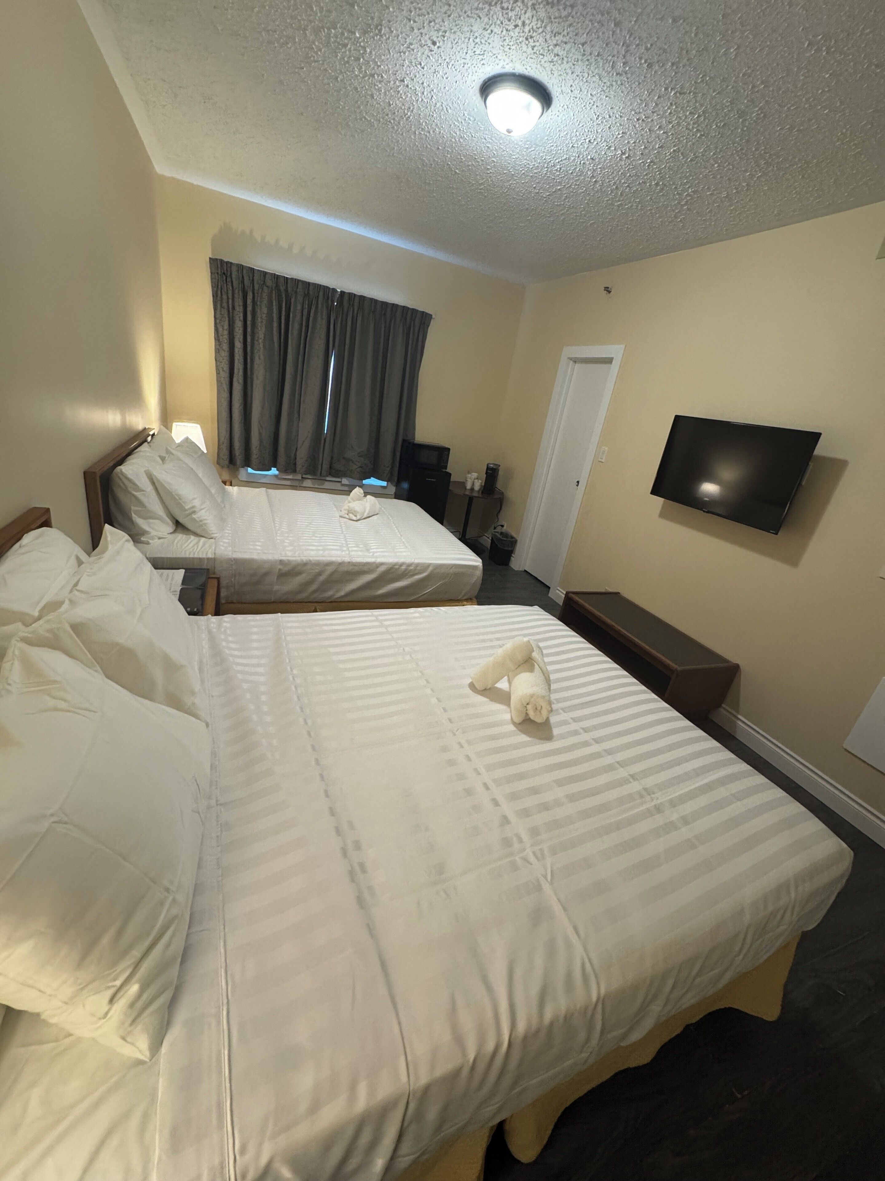 A hotel room with two beds, a flat-screen TV mounted on the wall, and a window with curtains.