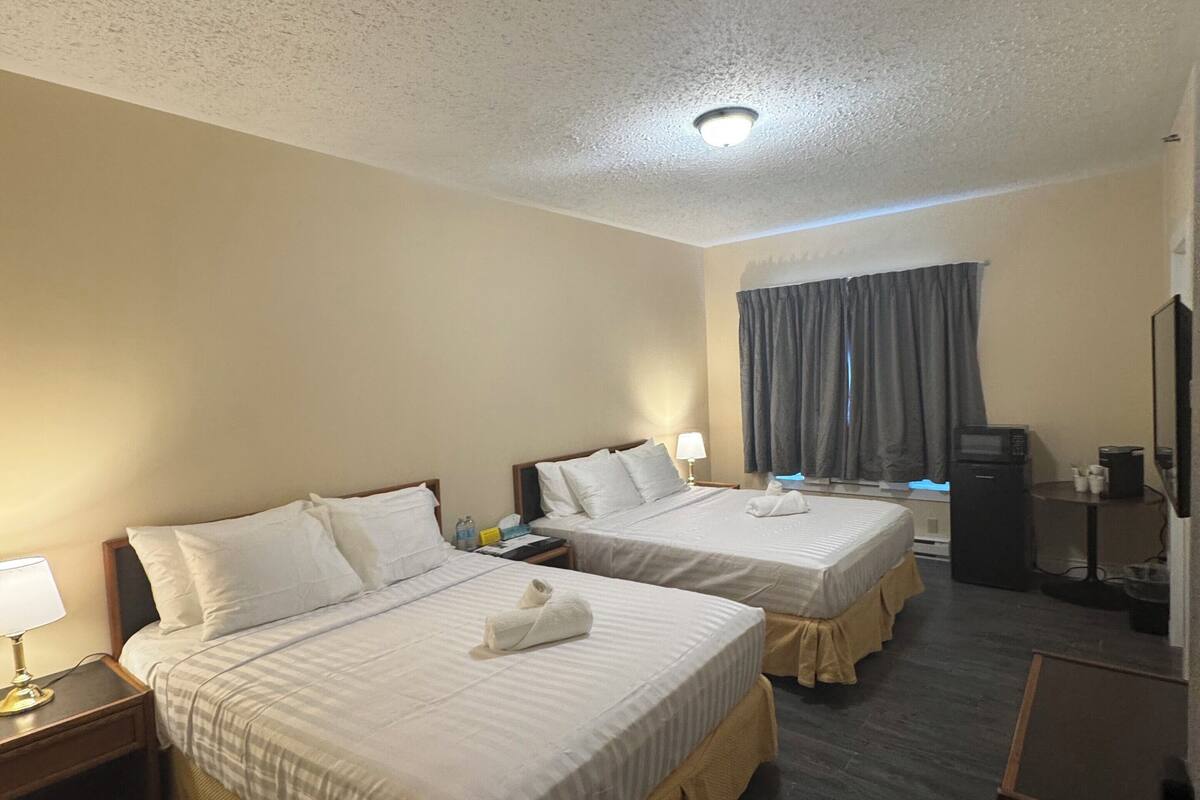 A hotel room with two beds, a desk, a television, and a microwave.