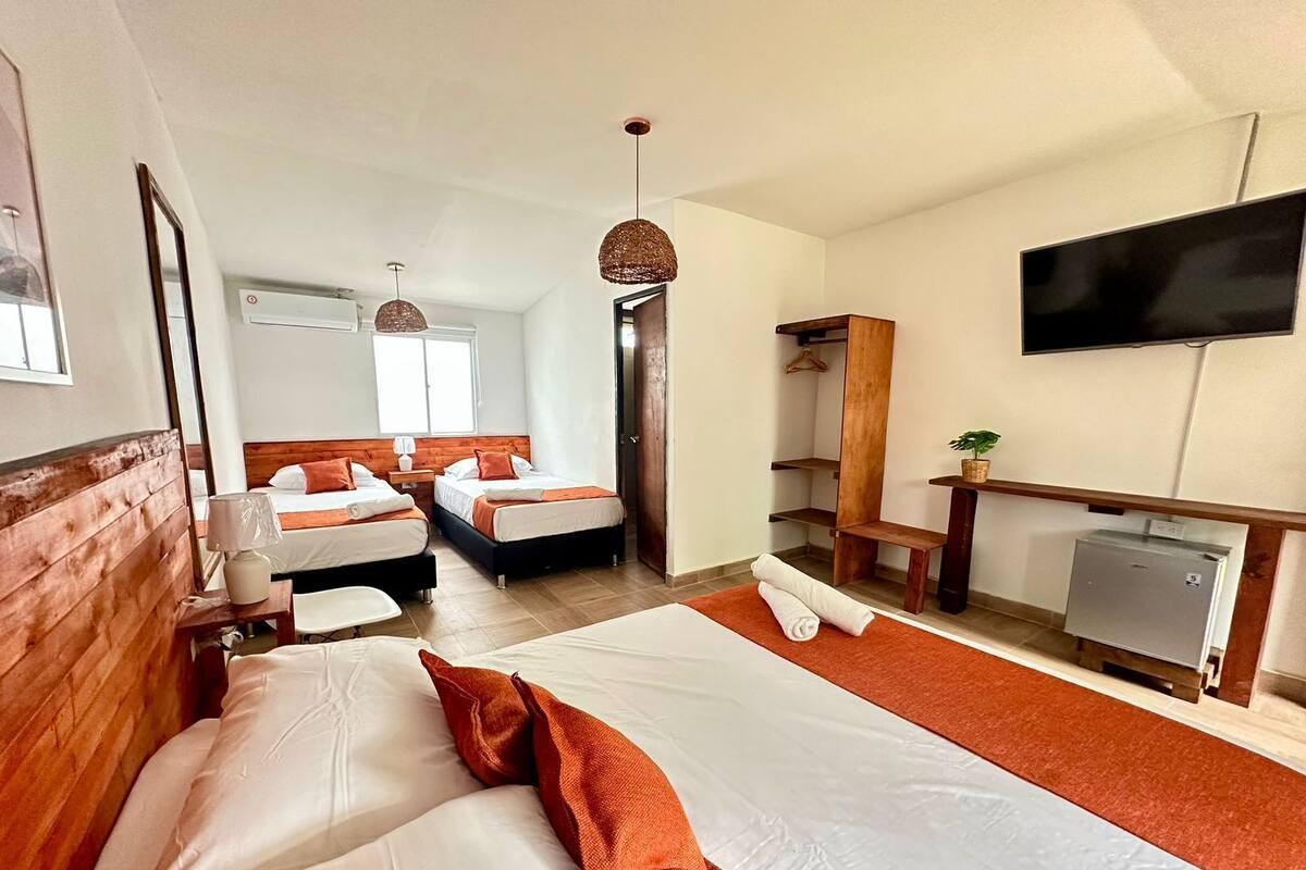 A hotel room with two beds, a TV, a desk, and a small kitchenette.
