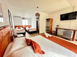 Habitación de hotel con dos camas, televisión, escritorio y una kitchenette pequeña.