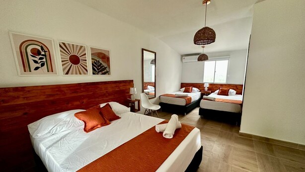 A modern hotel room with a large bed, two smaller beds, a desk, and a mirror. - eco hotel palma É coco (San Andrés)