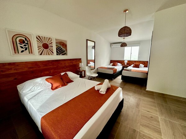 A modern hotel room with a large bed, two smaller beds, a desk, and a mirror. - eco hotel palma É coco (San Andrés)