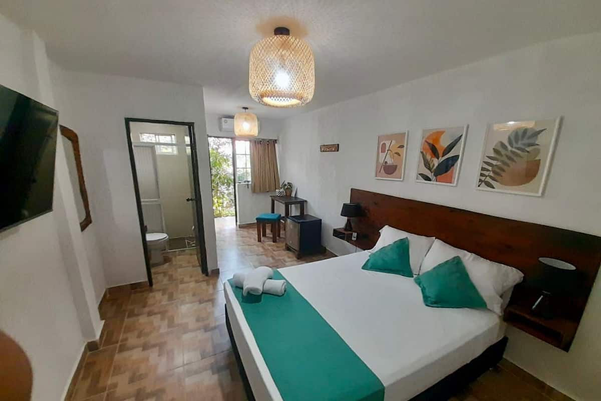 A hotel room with a large bed, a wooden headboard, a bedside table with a lamp, and a view of the outside through a glass door.