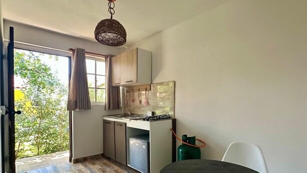Una cocina compacta con estufa a gas, un refrigerador pequeño y una zona de comedor con una mesa redonda y dos sillas.