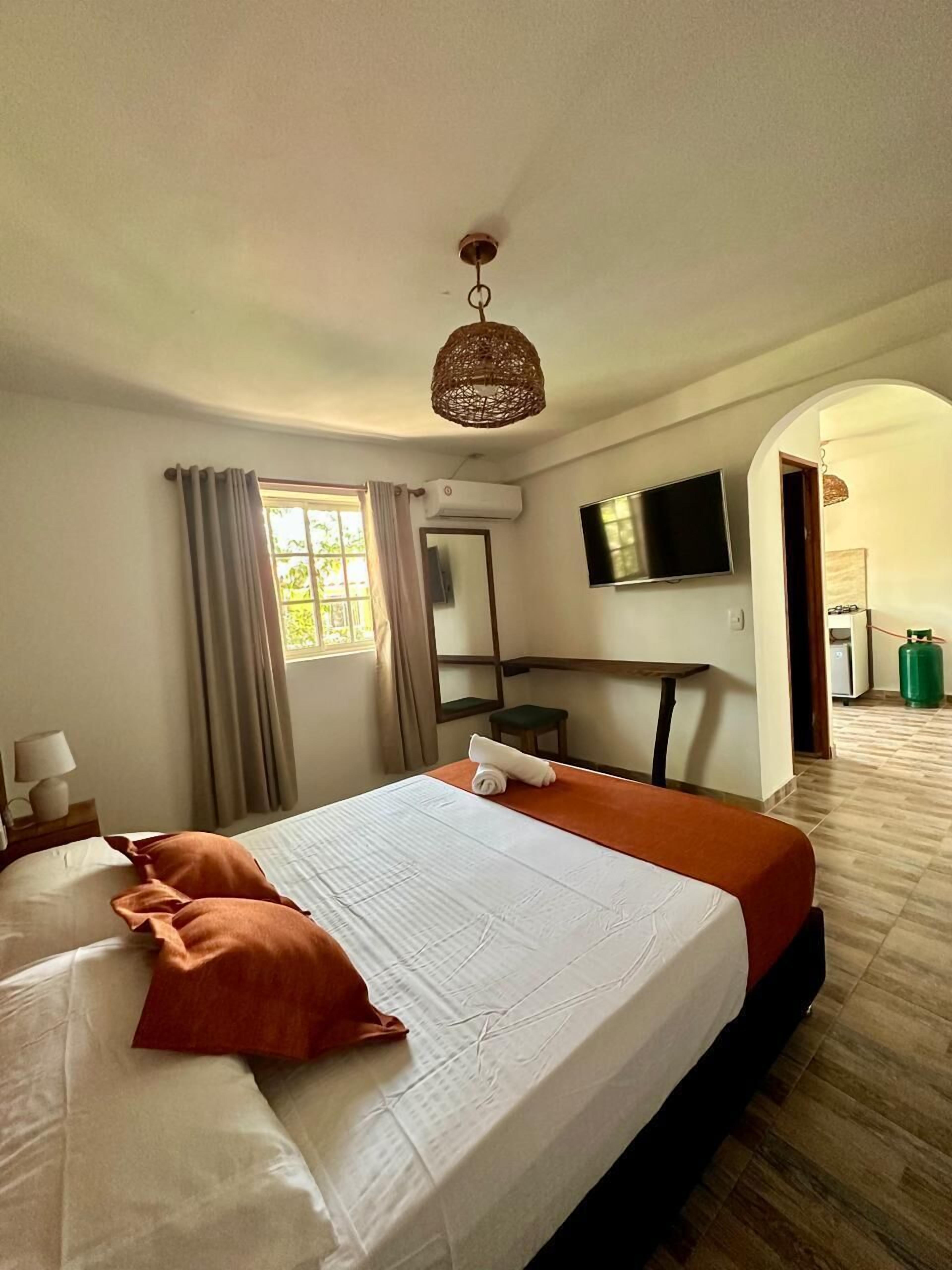 A hotel room with a large bed, a television, a desk, and a mirror.