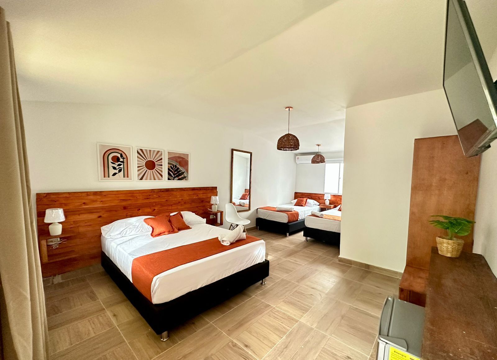 A hotel room with a large bed, two smaller beds, a desk, and a TV.