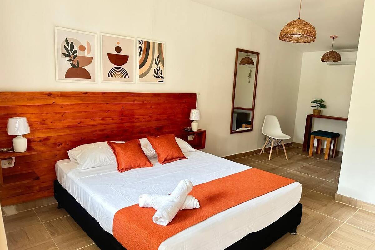 A neatly made bed with white and orange bedding, a wooden headboard, and a white nightstand with a lamp.