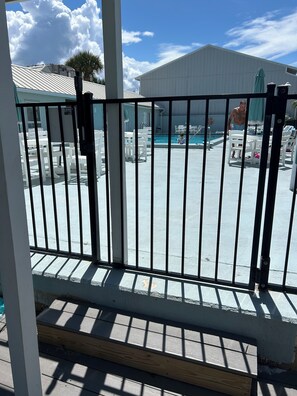 A pool area with white chairs and tables, a clear sky, and a building in the background.