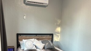 Una camera da letto con un letto, un comodino, un condizionatore d'aria e un pannello di controllo a parete.