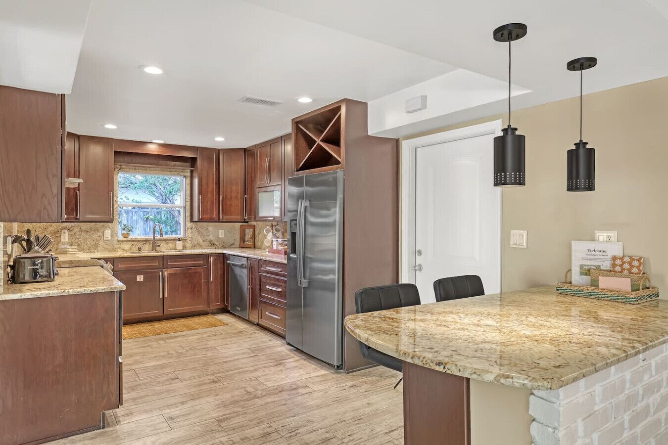 A modern kitchen with wooden cabinets, a stainless steel refrigerator, and a granite countertop.
