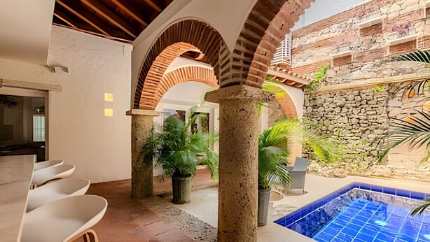 A modern interior with a pool area, featuring a stone wall, arched columns, and a tiled pool. - Casa Bovedas - 5 Bedroom Paradise (Cartagena de Indias)