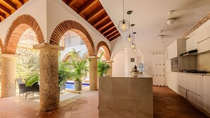 A spacious kitchen with a central island, wooden beams, and a stone column. - Casa Bovedas - 5 Bedroom Paradise (Cartagena de Indias)