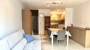 A modern living room with a sofa, dining table, and chairs. There is a kitchen area with cabinets and a countertop. - Apartment in Middelkerke Near the Beach (Middelkerke)