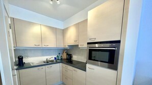 A modern kitchen with light-colored cabinets, a stainless steel oven, and a black microwave. - Apartment in Middelkerke Near the Beach (Middelkerke)