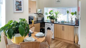 A compact kitchen with a dining area, a washing machine, and a large potted plant. - 3 bedroom accommodation in Brecon (Brecon)