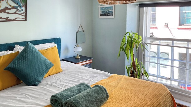 A neatly made bed with a yellow and blue headboard, a rolled-up towel, and a plant beside a window. - 3 bedroom accommodation in Brecon (Brecon)