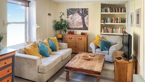 A living room with a sofa, coffee table, and a television. There is a bookshelf with books and a plant. - 3 bedroom accommodation in Brecon (Brecon)
