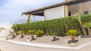 Een modern gebouw met een plat dak, een overdekt terras en een goed onderhouden tuin met diverse planten en een decoratieve muur.