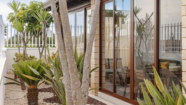 Een modern gebouw met grote glasramen, een stenen gevel en een buiten zitgedeelte met planten.