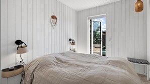 Een slaapkamer met een bed, nachtkastje, lamp, wanddecoratie en uitzicht door een geopende deur.