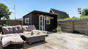 Een klein houten huis met een balkon, een bank en een tafel met een fruitschaal.